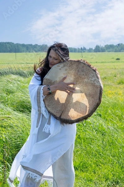 Fototapeta Female shaman in the white dress drumming outdoors