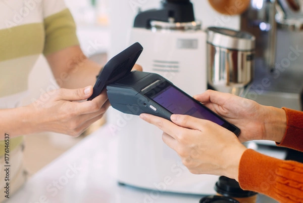 Fototapeta Asian woman paying for purchase with mobile phone at coffee shop. Contactless payment at cafe restaurant. Customer using NFC Smartphone making payment, paying on terminal. Cashless payment technology.