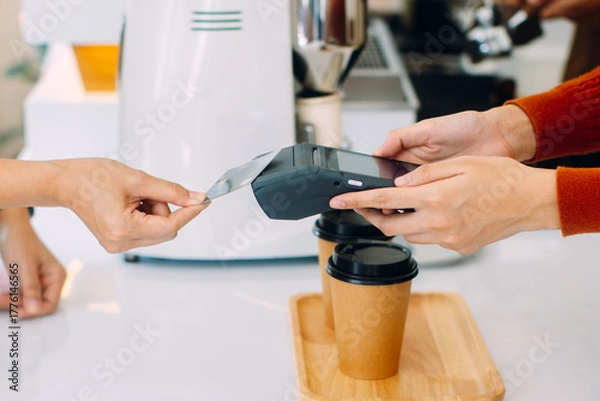 Fototapeta Contactless payment, Customer using credit card for making payment at cafe restaurant. Close up of woman using card for paying , shop owner receiving payment from customer in coffee shop.