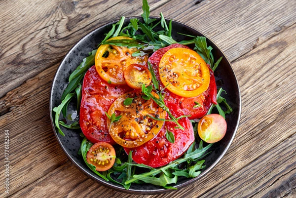 Fototapeta Organic Heirloom Tomato salad in a plate with salt and arugula on wooden background top view