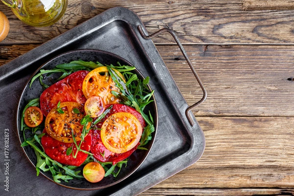 Fototapeta Organic Heirloom Tomato salad in a plate with salt and arugula on wooden background top view copy space for text