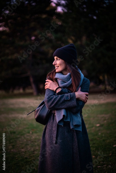 Obraz Confident and attractive woman wearing warm knitted scarf and beanie while standing in the park in an autumn day