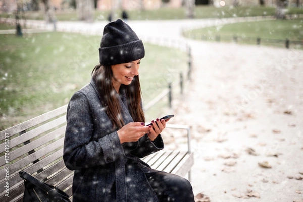 Obraz Woman sitting on a bench and enjoying the snow in the city park