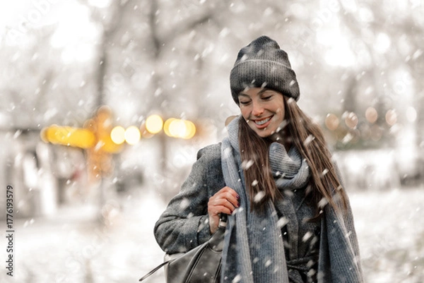Obraz Cheerful smiling woman standing in the snowfall at the park