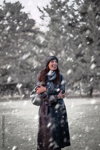 Obraz Cheerful smiling woman standing in the snowfall at the park