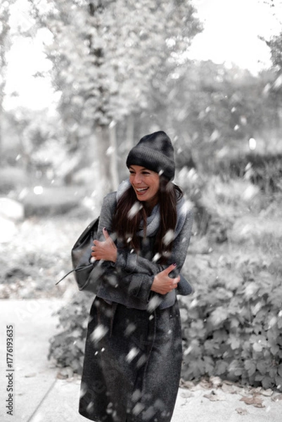 Obraz Cheerful smiling woman standing in the snowfall at the park