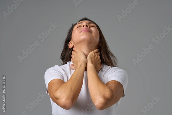 Fototapeta Woman holding neck in pain and looking up showing tension or discomfort in throat area indoors