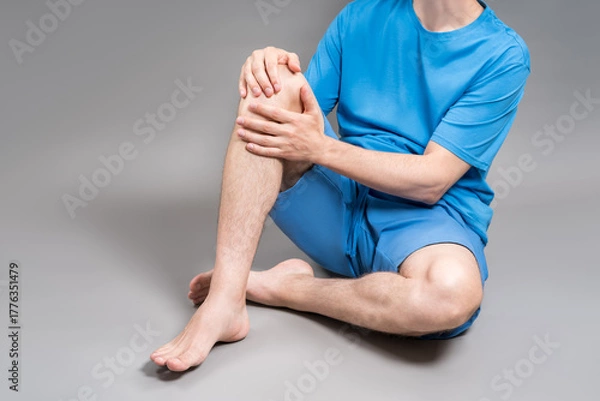 Obraz Knee pain, joint inflammation, arthritis and degenerative changes, man suffering from leg ache and doing self-massage on gray background