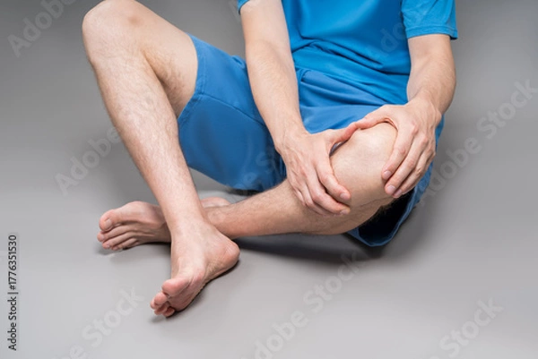 Obraz Knee pain, joint inflammation, arthritis and degenerative changes, man suffering from leg ache and doing self-massage on gray background