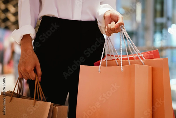 Obraz Close-up of a person holding multiple shopping bags in a mall, symbolizing retail therapy, consumerism, and modern lifestyle.