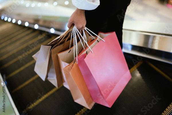 Fototapeta Close-up of a person holding multiple shopping bags in a mall, symbolizing retail therapy, consumerism, and modern lifestyle.