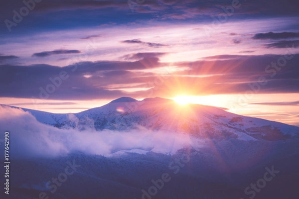 Fototapeta Beautiful sunrise in the winter mountains. Dramatic cloudy over sky. View of foggy hills  and trees covered with rime. Filtered image:cross processed retro effect.
