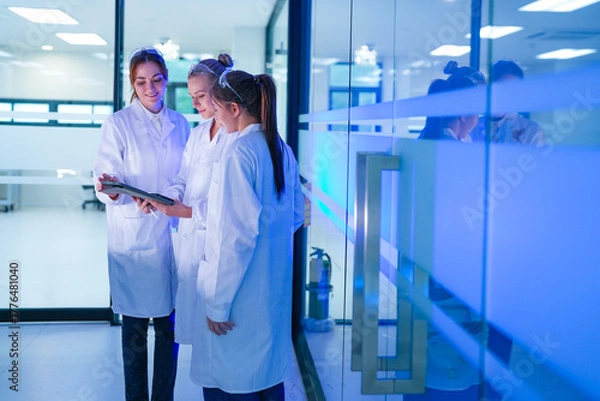 Fototapeta A diverse team of researchers in a biotechnology lab reviews preliminary data from an experiment on a tablet. They are collaborating on the next phase of their R&D project.