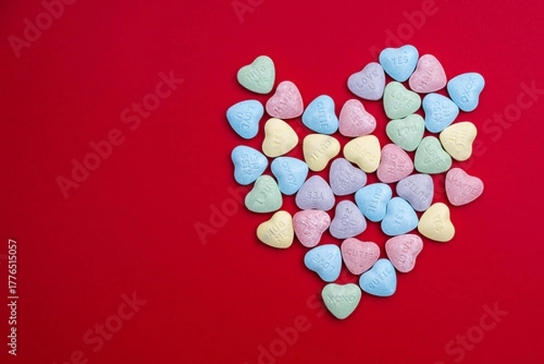 Fototapeta Pastel candy conversation hearts in a heart shape on a red background.  Valentine's Day background