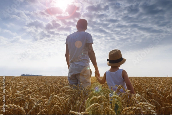 Fototapeta Father and son look at the sun. Weat field. Backview.