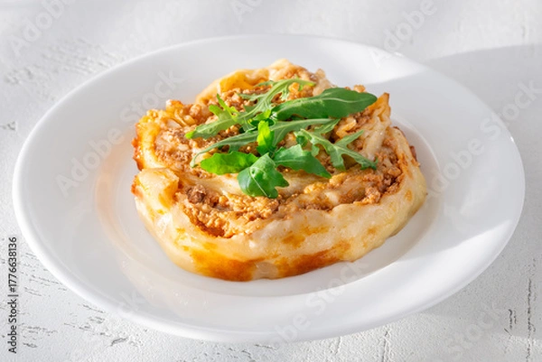 Fototapeta Circular lasagna presentation topped with fresh arugula served on elegant white plate