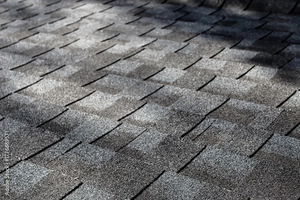Fototapeta close-up of an asphalt shingle roof at an angle with dappled sunlight. gray tones abstract texture background. construction and architecture banner. aerial view with copy space. architectural roofing.