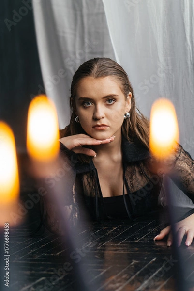 Fototapeta Mysterious young woman in black lace gazes intensely through candlelight, evoking elegance and gothic allure