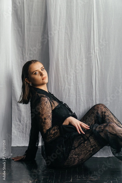 Fototapeta Mysterious young woman in black lace gazes intensely through candlelight, evoking elegance and gothic allure