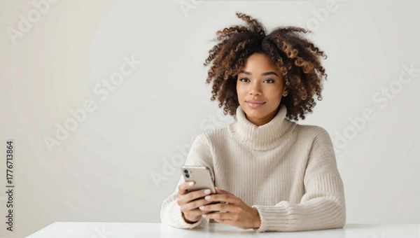 Fototapeta Girl with curly hair sits at table using smartphone