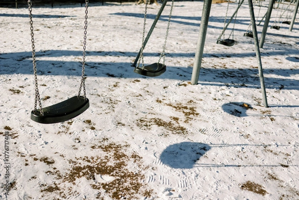 Fototapeta Empty swings sway in the winter snow at a local park during the afternoon
