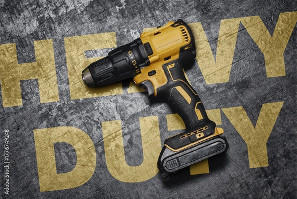 Fototapeta Yellow cordless drill lies on a rough concrete surface with bold yellow Heavy Duty text. Concept of professional power tools, construction, repair, and durable industrial equipment for heavy work.