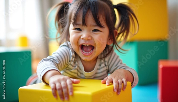 Obraz Joyful toddler girl playing with colorful cubes, smiling happily and laughing in playroom. Toddler girl enjoys playing time, showing vibrant emotions and playful spirit.