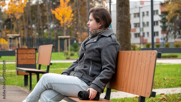Fototapeta Woman Sitting on a Park Bench Holding a Camera During Autumn in the City