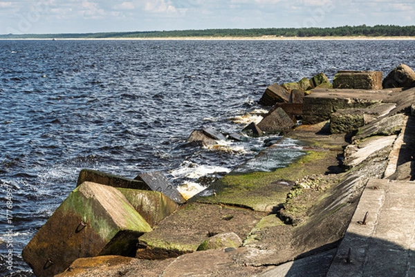 Fototapeta Concrete breakwater on the seashore, waves hitting the blocks