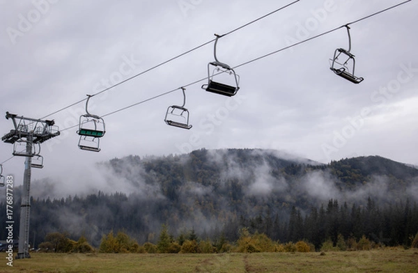 Fototapeta Ski lift without people on the background of mountains, clouds and fog