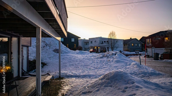 Fototapeta A quiet residential neighborhood in city of Tromsø, Norway with houses. Roads are covered in deep winter snow during a soft pastel sunset.