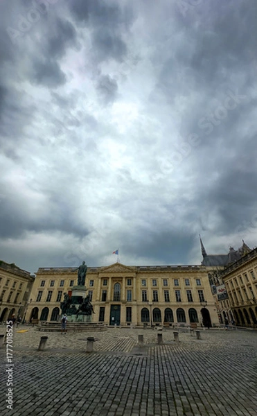 Fototapeta Reims, Marne, Grand-Est, France, August, 28th, 2025, Champagne Area, A magnificent and imposing building stands proudly in a historic square, surrounded by gloomy, overcast skies