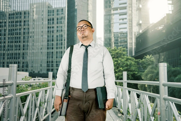 Obraz Serious Asian Businessman Commuting with Laptop and Bag on a Bridge Walkway in the City