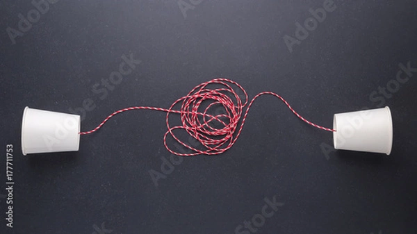 Fototapeta Two white paper cup connect with red rope used for classic phone on black stone table board. For old communication system concept