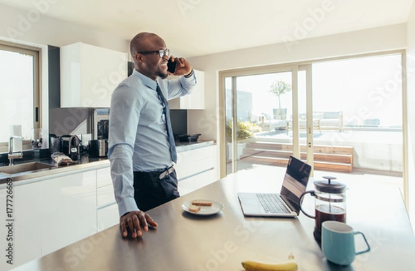 Fototapeta Man talking over phone while having breakfast