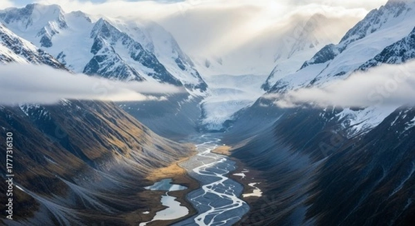 Obraz Dramatic aerial view of a glacial valley, snow-capped peaks, river, clouds, and sunlight