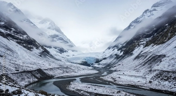 Obraz A winding river flows between snowy, mountainous terrain, leading towards a glacier under a cloudy sky