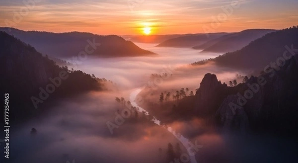 Fototapeta Aerial view of a river winding through valley, shrouded in mist, bathed in warm sunset hues