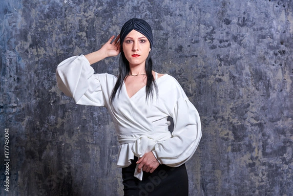 Obraz In a dark room stands a beautiful girl with long hair, dressed in a black leather skirt and a white blouse. Her outfit is designed in a business style. This is the image of a business woman.
