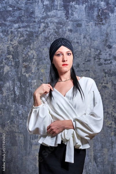 Obraz In a dark room stands a beautiful girl with long hair, dressed in a black leather skirt and a white blouse. Her outfit is designed in a business style. This is the image of a business woman.