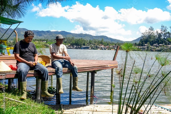 Fototapeta Tranquil Lakeside Scene Shows Two Men Enjoying Peaceful Moment Together While Fishing