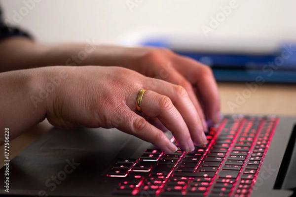 Fototapeta Close-up of a businesswoman working late typing on a blue backlight, backlit on laptop keypad.Anonymity on the Internet can provide benefits in terms of privacy and freedom of expression