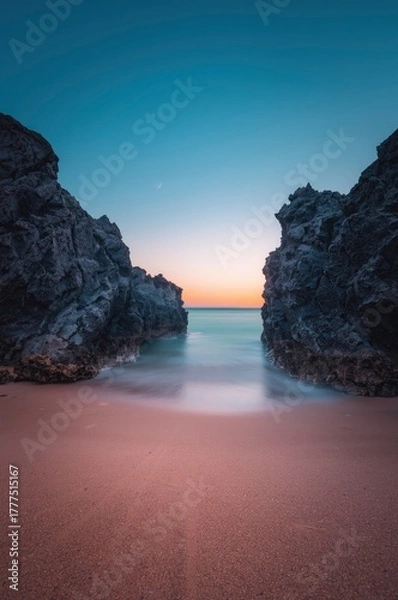 Fototapeta A captivating coastal landscape unfolds at twilight, featuring rugged, dark rock formations that majestically frame a tranquil expanse of water. The sky above presents a stunning gradient, transitioni