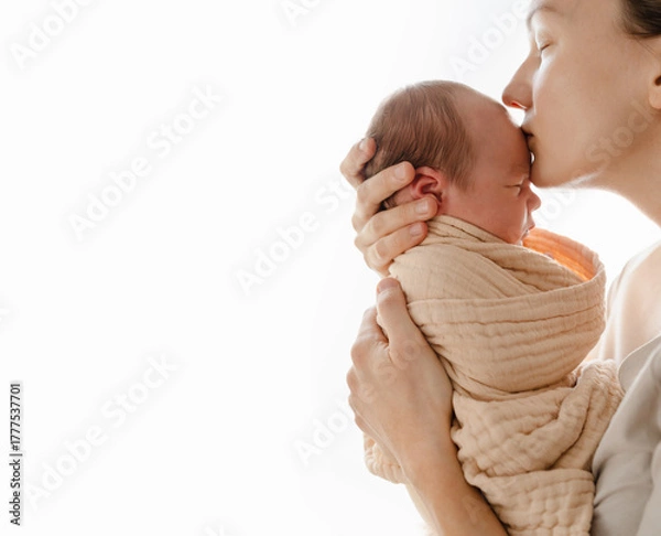 Fototapeta Beautiful mother kissing her baby. Authentic photography of mother holding her newborn baby after labor. Newborn in mother's hands. Baby care. Childbirth and motherhood concept.