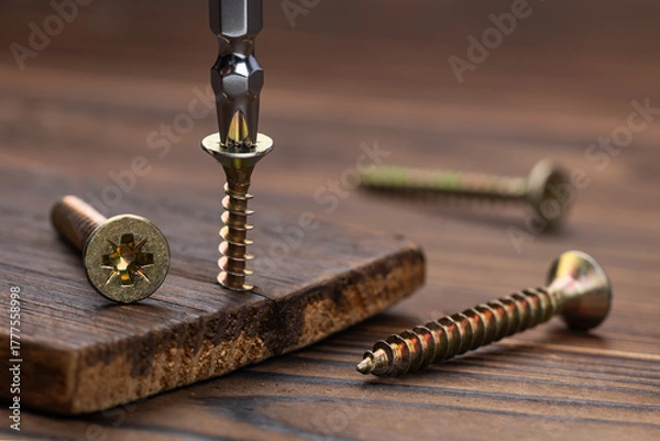 Fototapeta Screwdriver on the screw, screw screwed into timber wood, screw on wooden top table. Close-up, selective focus
