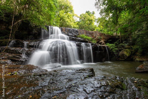Fototapeta Serene Waterfall Scene: Witness the mesmerizing cascade of water tumbling gracefully over ancient stones, creating a tranquil oasis within a lush green forest, inspiring peace and serenity.