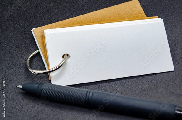 Obraz Close up of white banner shape notepad with customizable space for text on black cover background and with black pen.