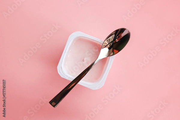 Fototapeta Strawberry yogurt or pudding  in white plastic cup on pink background with copy space. Strawberry pink yoghurt with spoon on it. Minimal style. Flat lay, top view.