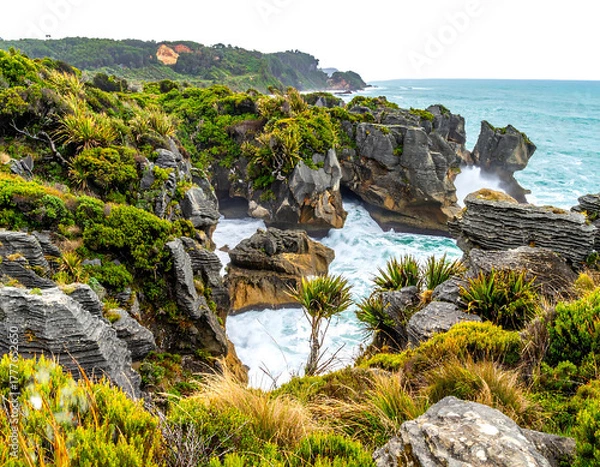 Obraz A coastal scene showcases dramatic rock formations carved by the ocean. Lush greenery clings to the rugged cliffs, contrasted by turbulent waves