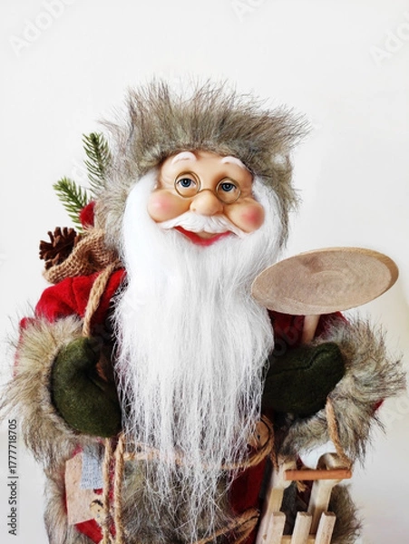 Obraz A Christmas toy in the form of Santa Claus with a white beard and glasses, wearing a hat and coat. The atmosphere of celebration, comfort and winter fun. A holiday card for the New Year holiday.
